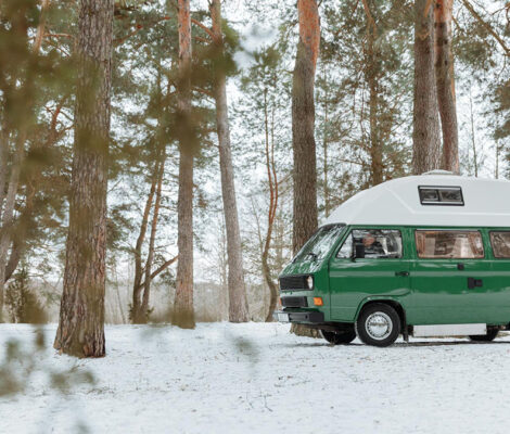 Furgoneta camper verde estacionada entre pinos nevados, preparada para viajar en invierno con calefacción estacionaria camper.