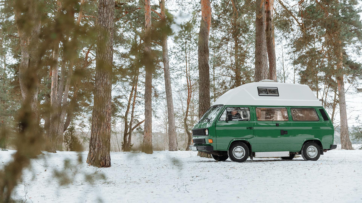 Furgoneta camper verde estacionada entre pinos nevados, preparada para viajar en invierno con calefacción estacionaria camper.